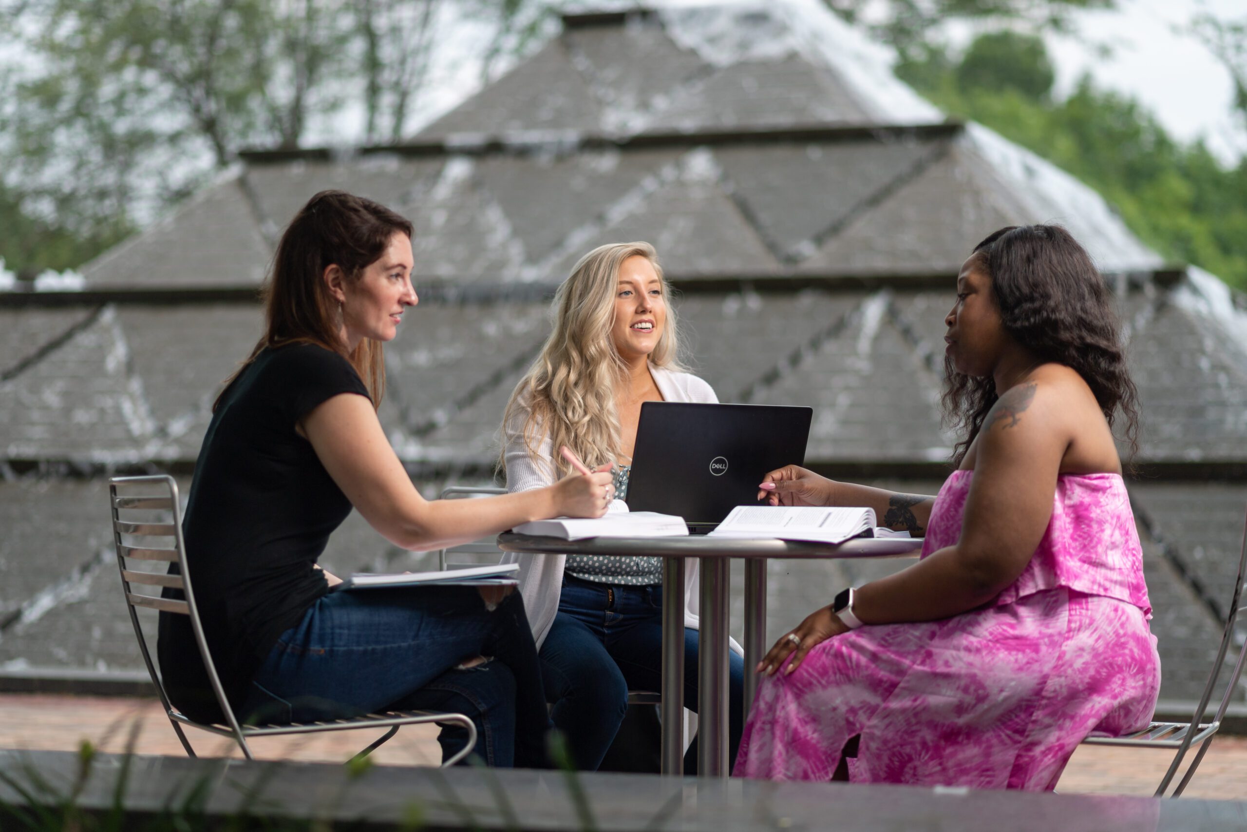 A group of three students collaborate outside next to a fountain